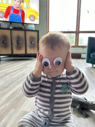 a toddler wearing gray and white pajamas with two googly eyes stuck over his eyes