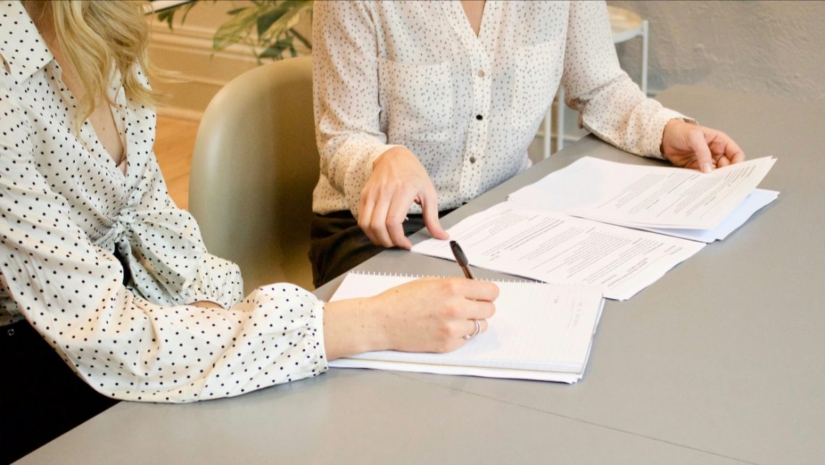 a tutor helping a student at a desk with a pen and paper