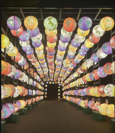 An illuminated tunnel of hanging spherical lanterns in various colors and patterns, leading into darkness.