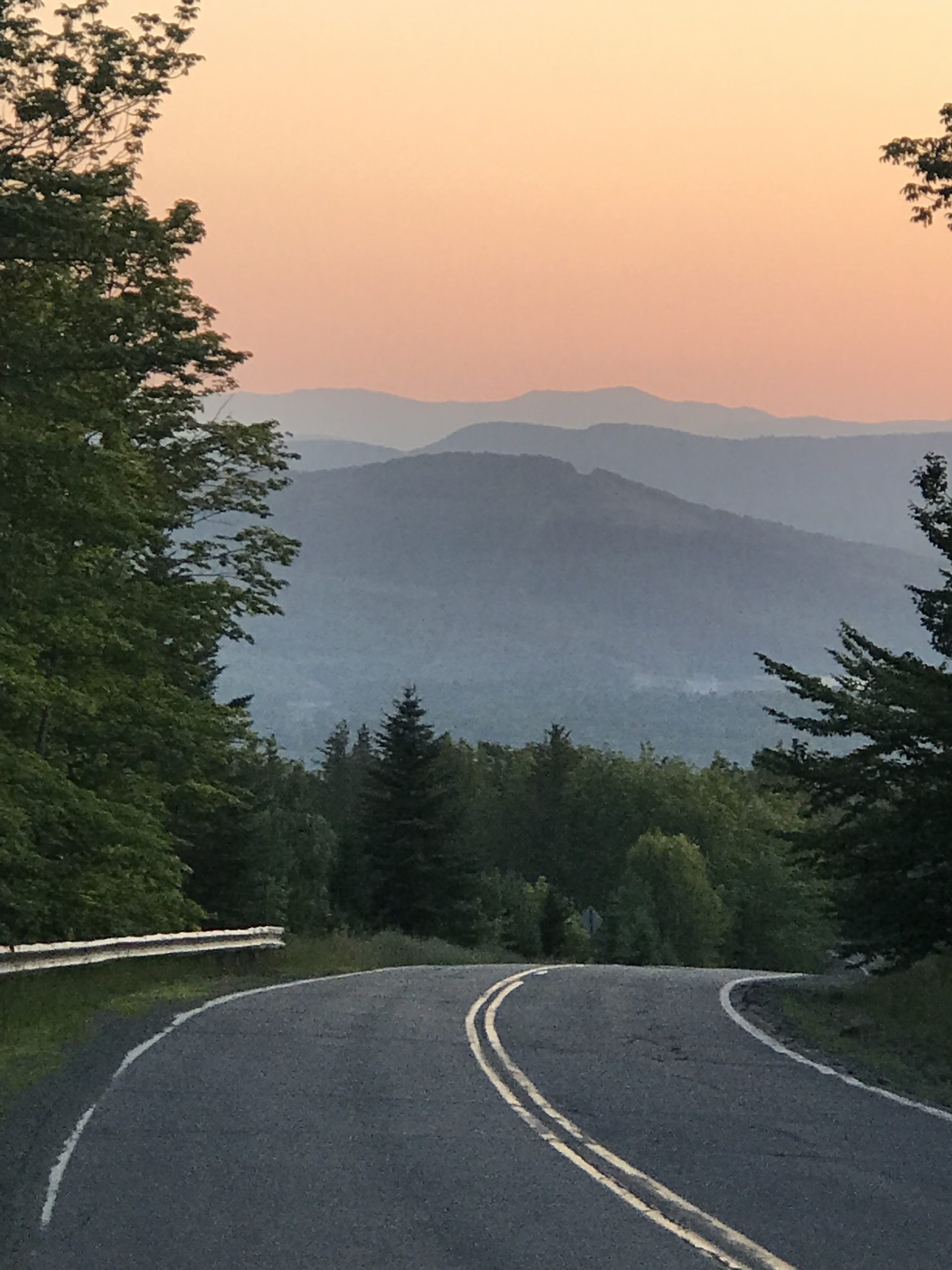 a serene landscape view during sunset. A curving asphalt road is in the foreground