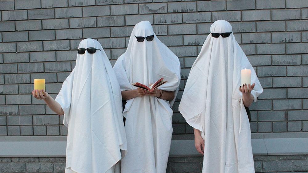 people in sheet ghost attire wearing sunglasses and holding candles