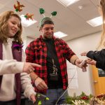UMA students decorating holiday wreaths with supplies like hot glue guns and red bows.