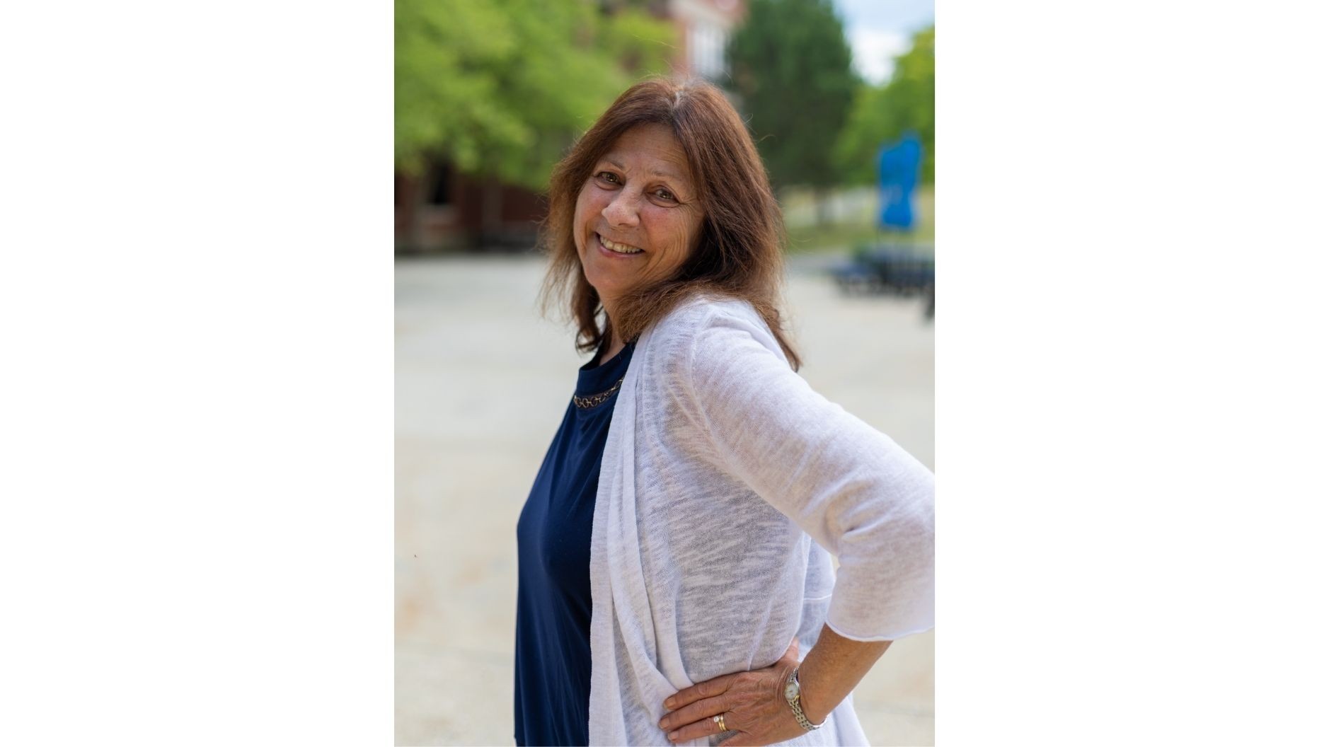 Amy Line smiles while standing outdoors on the UMA campus, wearing a navy top and light cardigan, with campus buildings and greenery softly blurred in the background.