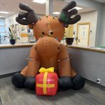 inflatable moose wrapped in holiday lights holding a present