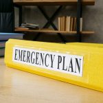 Yellow folder labelled "emergency" on a desk.