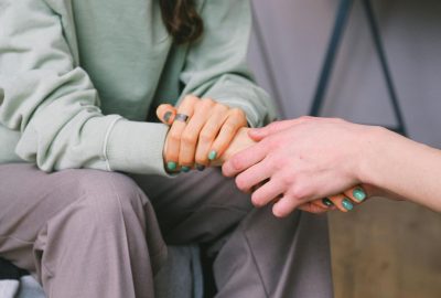 Close-up of seated person between shoulders and knees. Another person holds one of their hands.