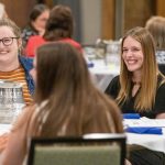Group of adults seated around a round table at a formal dinner, smiling and chatting during a graduate event.