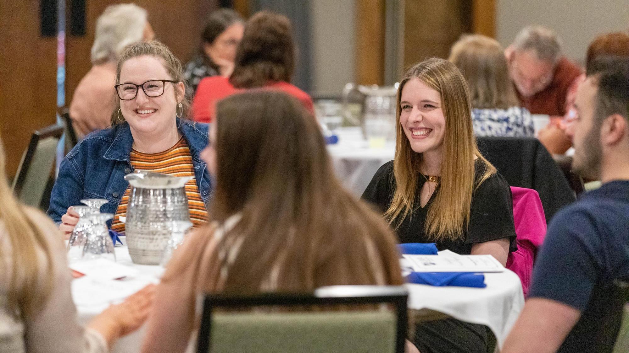 Group of adults seated around a round table at a formal dinner, smiling and chatting during a graduate event.