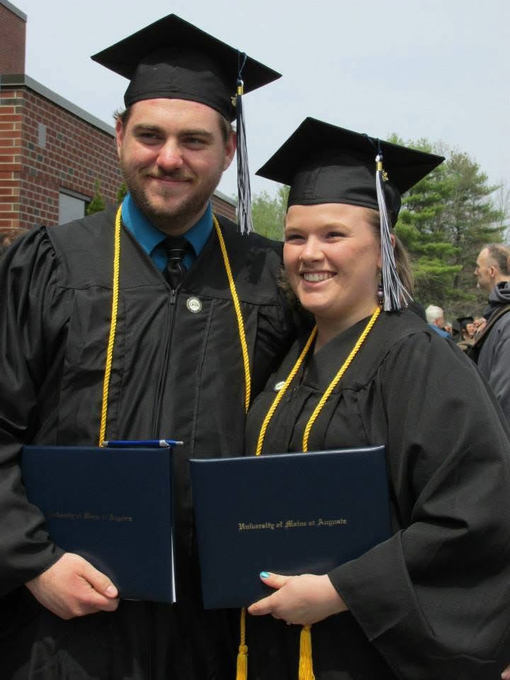 Matthew Knight and Christine McCormick Knight smile and pose for a picture in graduation caps and gowns, honor cords, and holding their UMA diploma covers.