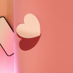 A smartphone lies on a pink gradient background, partially separated by a vertical shadow from a white heart shape on the right,