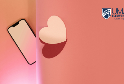 A smartphone lies on a pink gradient background, partially separated by a vertical shadow from a white heart shape on the right,