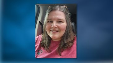 Allison Simpson, a woman with medium long hair held up with sunglasses smiles for the camera