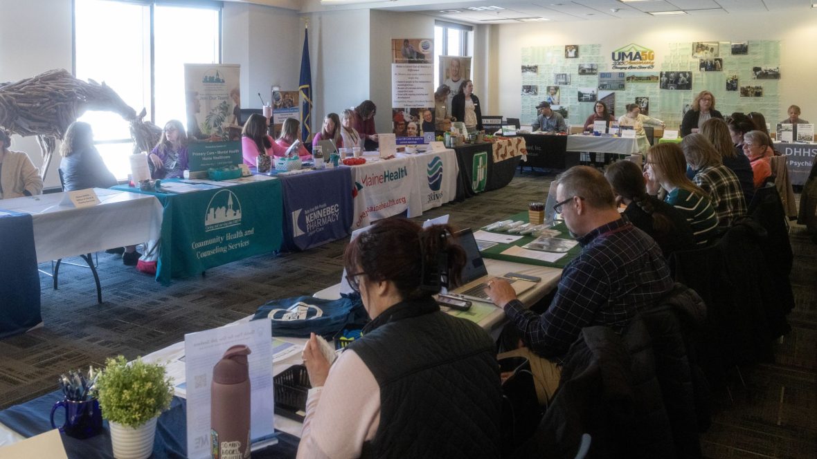 Employers sit at tables draped with banners showing their organization's name and logo, as they await the opening of UMA's 4th annual Job and Resource Fair.