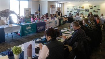Employers sit at tables draped with banners showing their organization's name and logo, as they await the opening of UMA's 4th annual Job and Resource Fair.