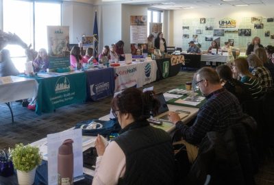 Employers sit at tables draped with banners showing their organization's name and logo, as they await the opening of UMA's 4th annual Job and Resource Fair.