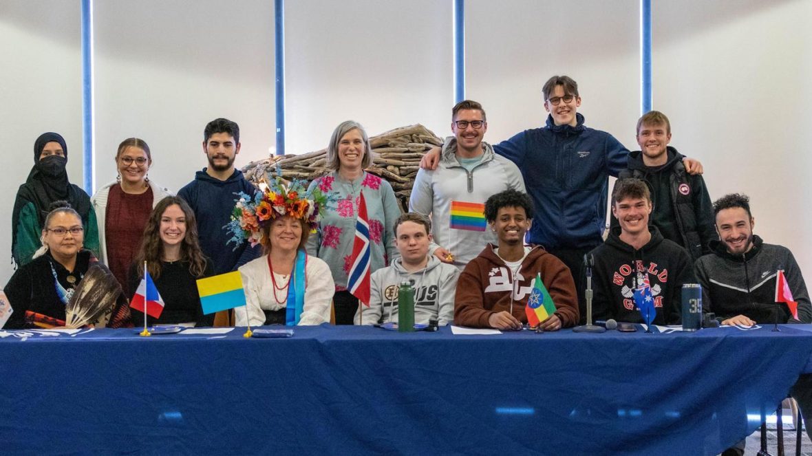 Students and staff pose together behind a table with international flags at a campus cultural celebration.