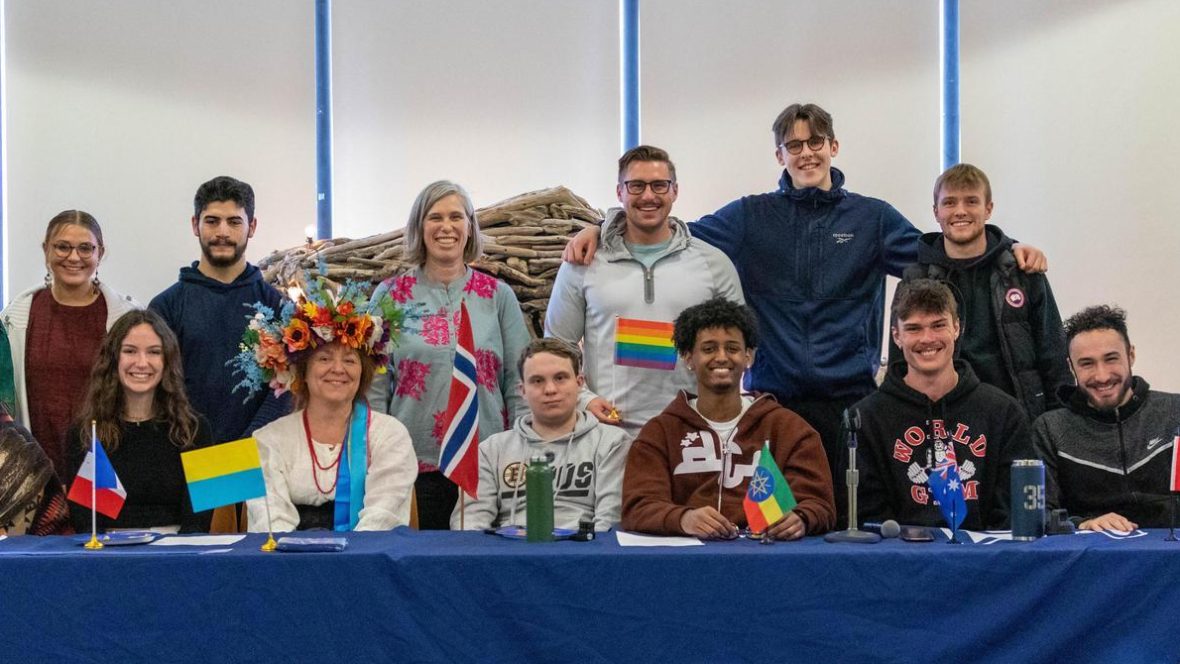 Students and staff pose together behind a table with international flags at a campus cultural celebration.