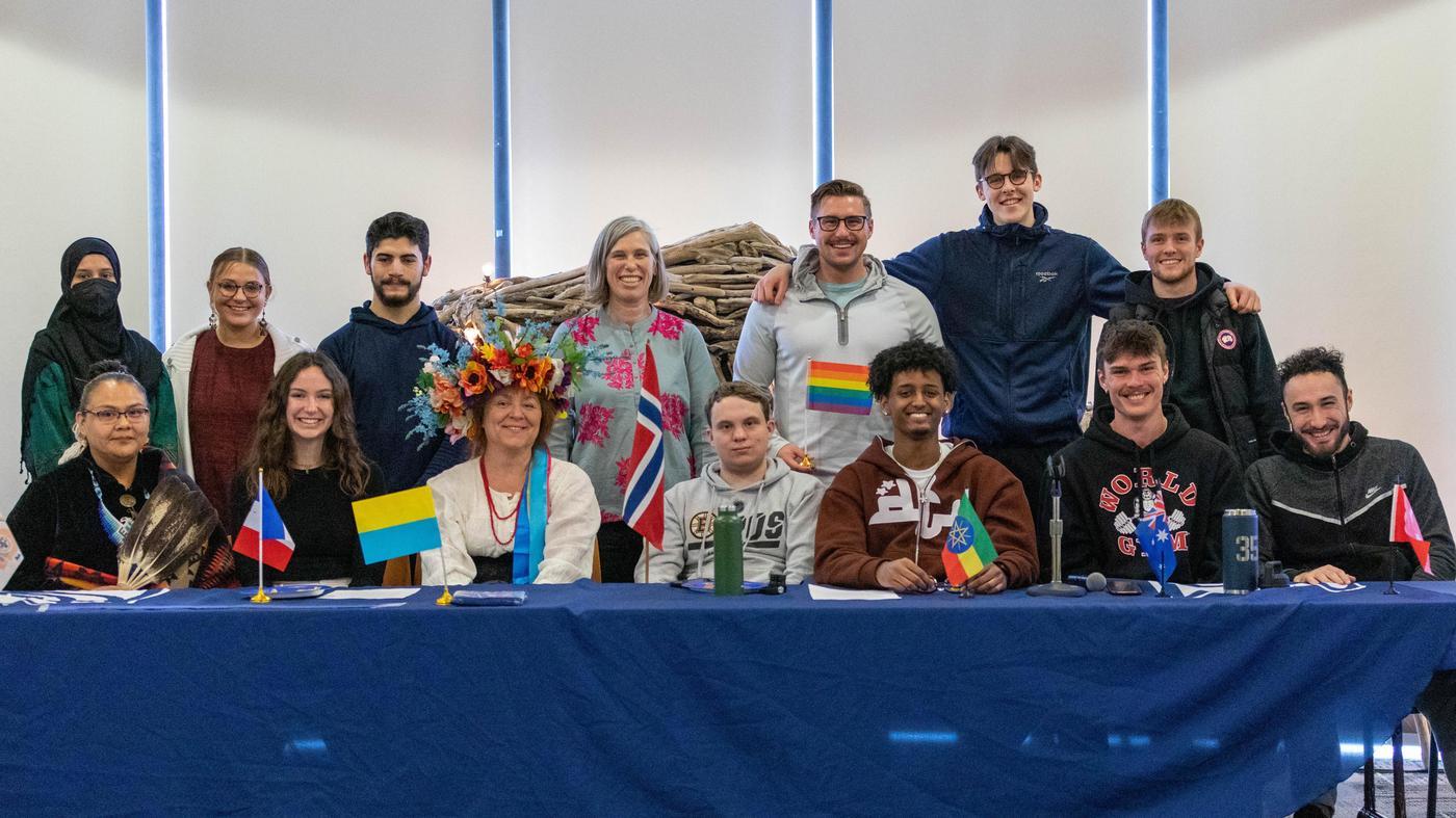 Students and staff pose together behind a table with international flags at a campus cultural celebration.