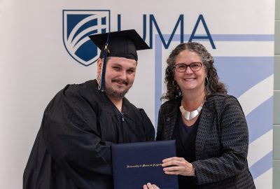 Travis Walker, 2025 UMA graduate, wears graduation regalia and poses with UMA President Jenifer Cushman as she presents Travis with his degree.