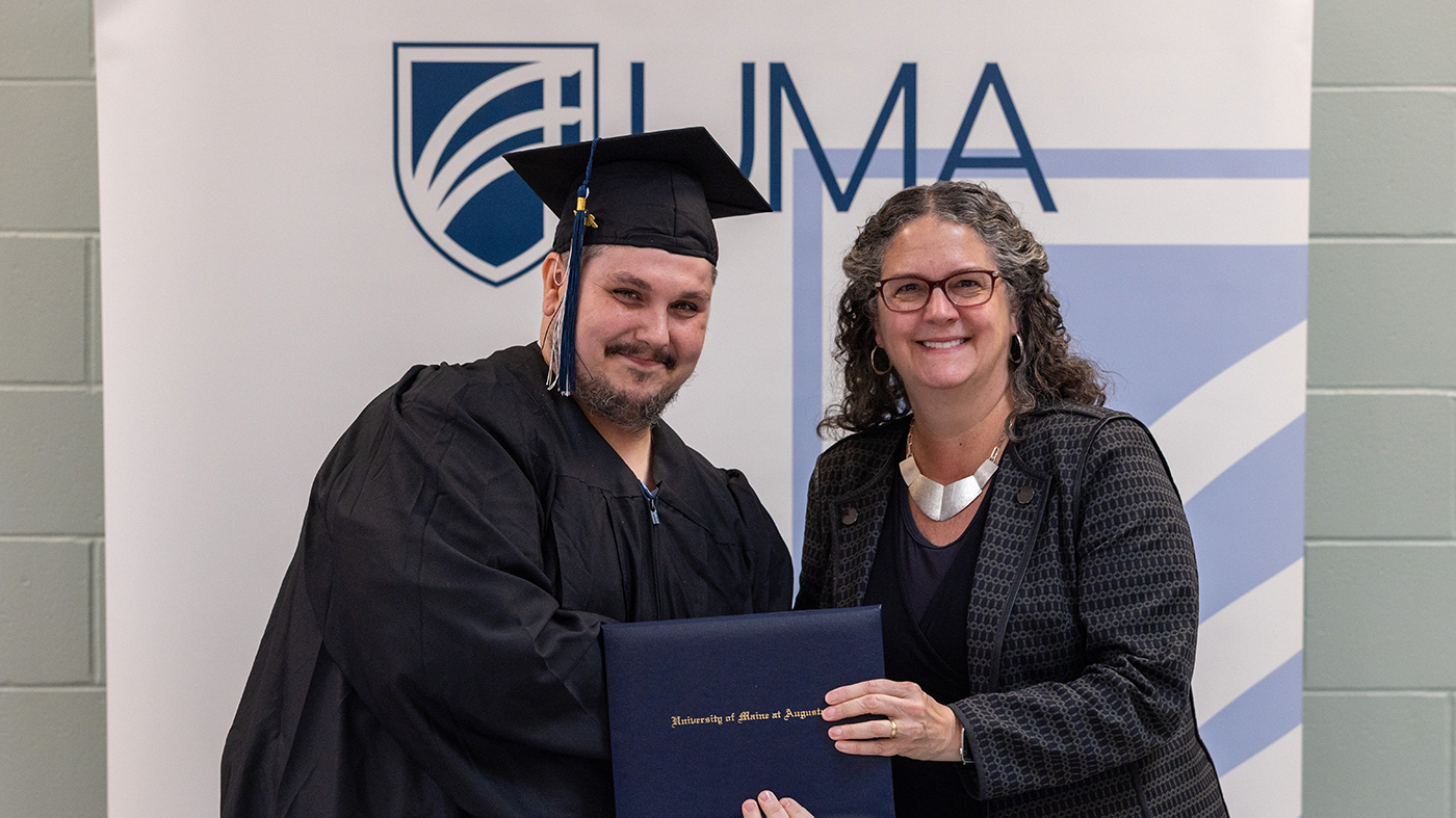Travis Walker, 2025 UMA graduate, wears commencement regalia and poses with UMA President Jenifer Cushman as she presents Travis with his degree.