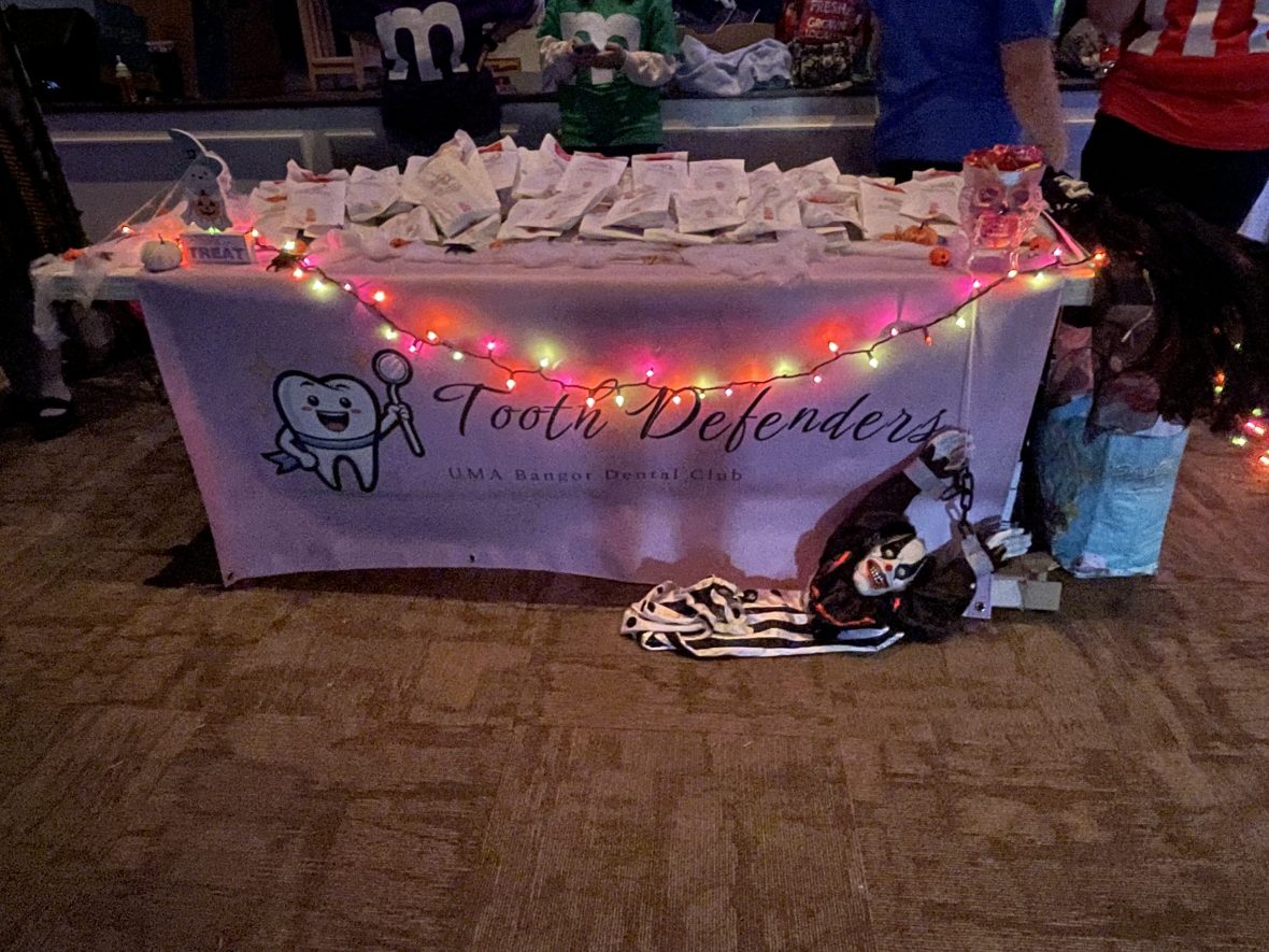 A decorated table for the “Tooth Defenders” UMA Bangor Dental Club featuring treat bags, colorful lights, and Halloween decorations.