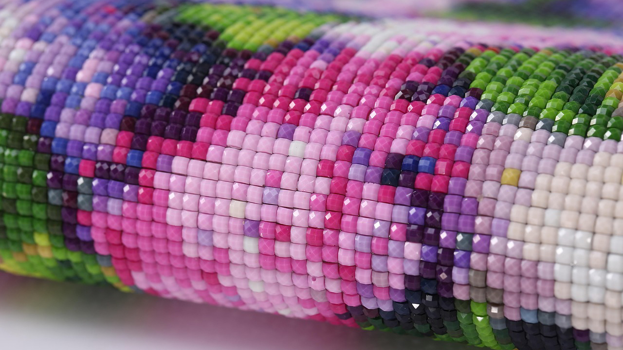 Close-up of a diamond painting showing small, faceted resin beads arranged in a colorful mosaic pattern with pink, purple, green, and white tones.