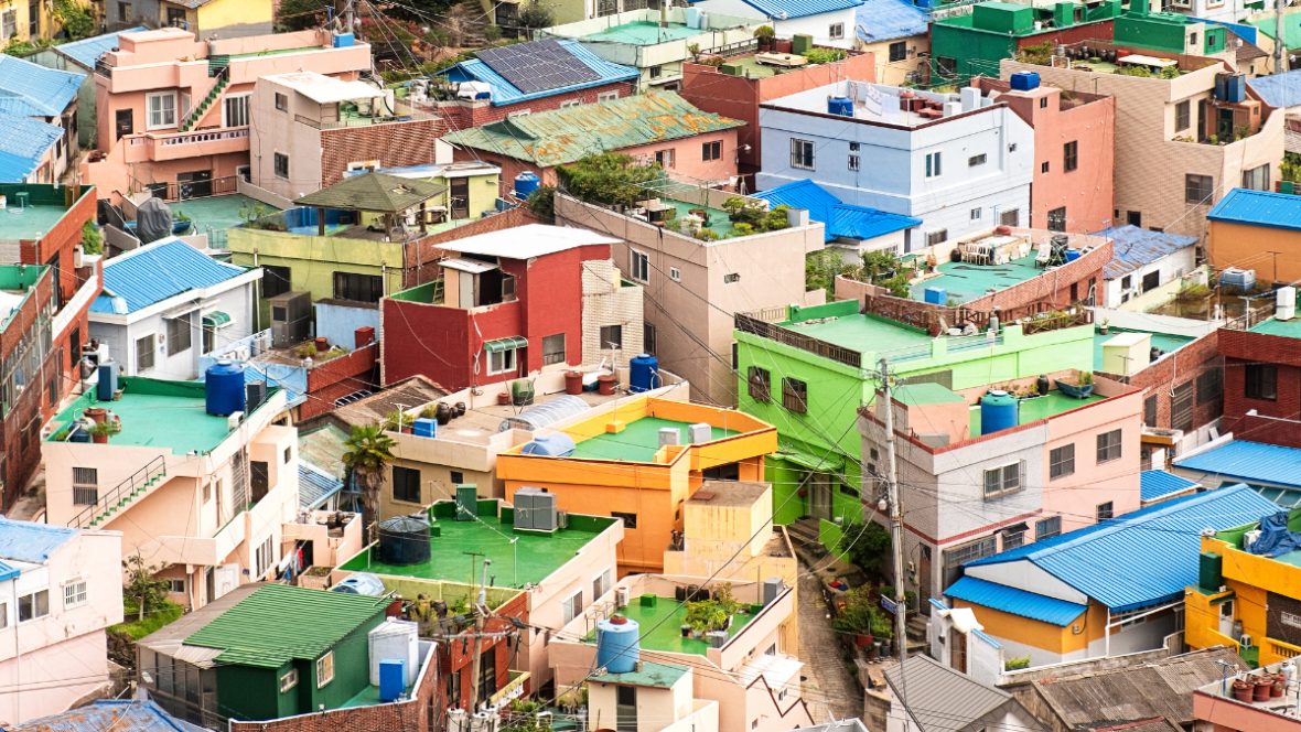 A densely packed hillside of colorful, multi-story buildings with bright blue roofs, in an urban coastal setting.