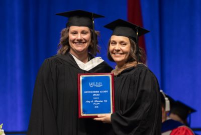 Amy Marston holding her Distinguished Alumni Award plaque presented by Kristen Eaton