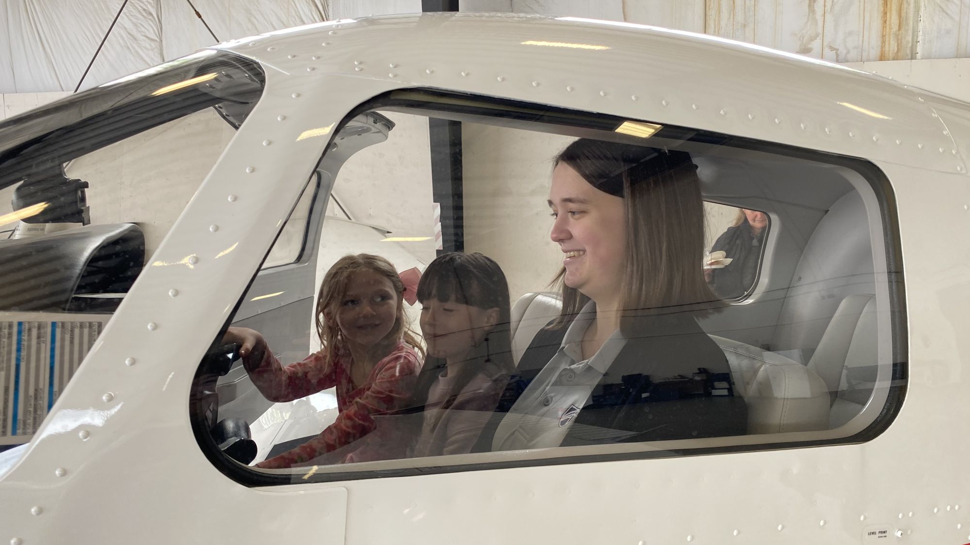 Casey Raymond shares her love of flying with two smiling young girls in the flight deck of a small airplane.