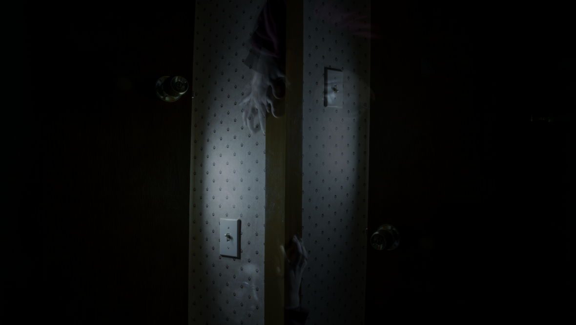 Very dark image of a corner with a creepy hand coming down from above and up from below.