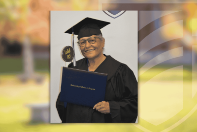 Mimi wearing a graduation cap and gown smiles while holding a University of Maine at Augusta diploma. She also holds a small sign that reads “I did it!”