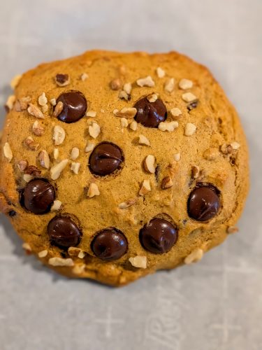 Close-up of a golden brown chocolate chip and walnut cookie. The chips form a smiley face