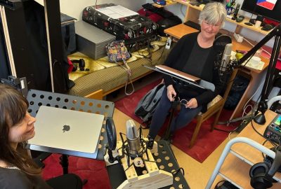Dr. Magda Nisponska and Dr. Sharon McMahon Sawyer record an episode of the Mentalizing Mediation podcast series in a small studio, seated near microphones, laptops, headphones, and audio equipment.