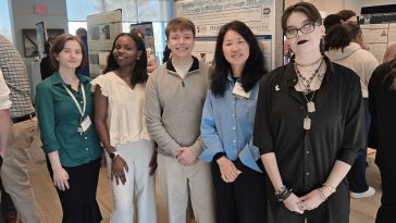 Five people stand together and smile in front of a research poster titled "Bridging Disciplines: Impacts of Environmental Chemicals on Physiology and Health 2026" at an academic symposium. From left to right: Emilie Robbins, Joana Massanga, Noah Lattig, Dr. Juyoung Shim, and Liz Avian Hollis.