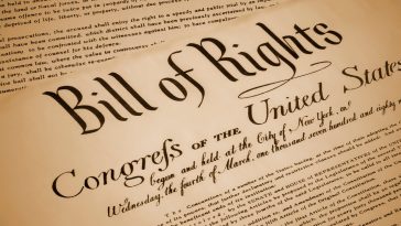 Close-up image of the Bill of Rights document, featuring large decorative lettering and portions of the handwritten text of the United States Constitution and amendments.