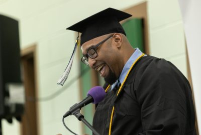 A man in graduation cap and gown addresses the audience at the 2026 UMA PEP commencement ceremony