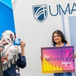 An accepted student posts at the UMA photo booth with a sign that days "The Adventure Begins."