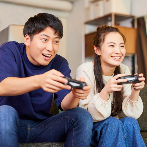A young couple enthusiastically playing a video game together on a sofa, both holding controllers and smiling.