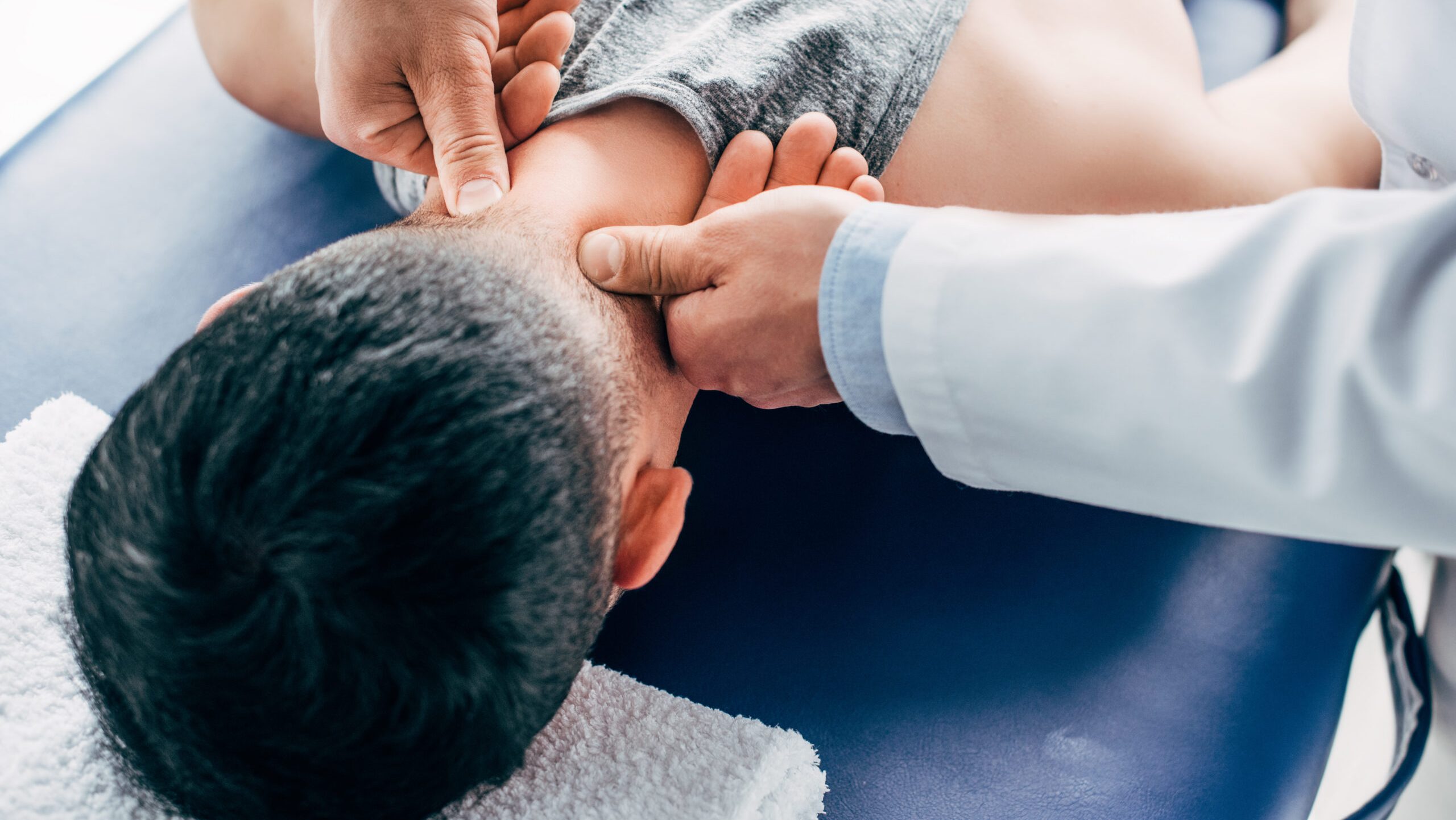 person laying face-down on a medical table, a provider pushes their thumbs along the back of their neck
