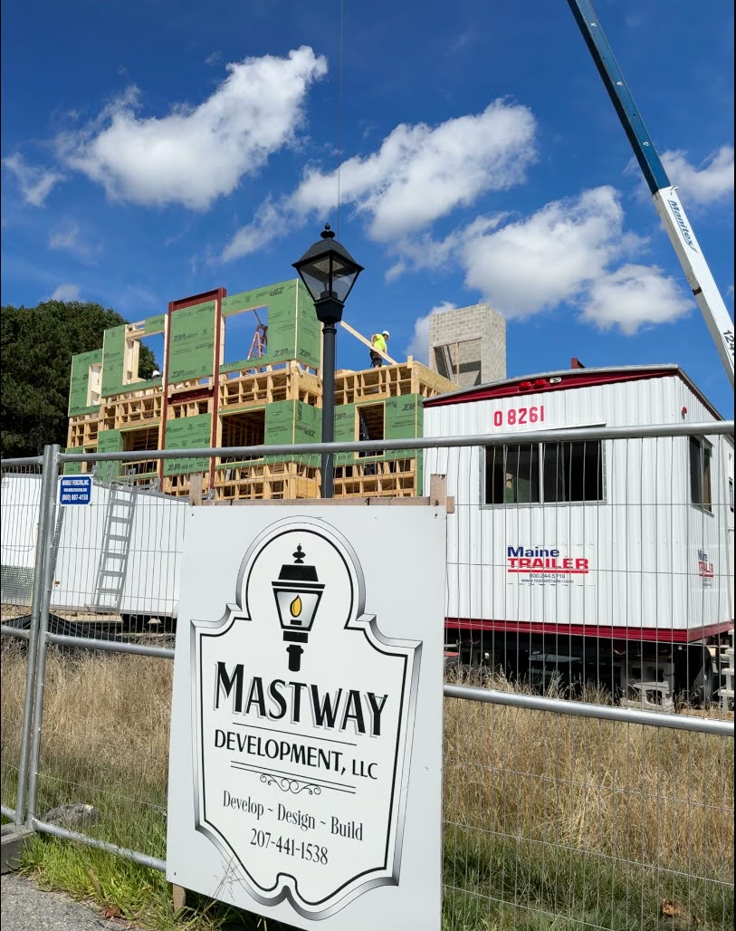 Closer view of Morrill Hall under construction, showing wood framing, green exterior sheathing, a crane, and the Mastway Development construction site sign in the foreground.