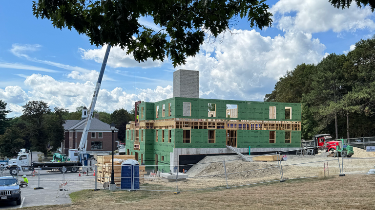 Construction progress on UMA’s new Morrill Hall residence hall, with the upper floors framed and sheathed as a crane and other equipment operate around the site.