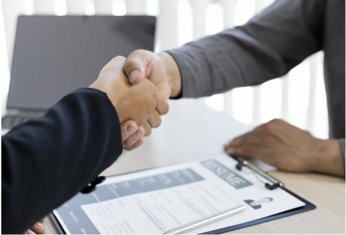 two people shaking hands over a clipboard in an office setting