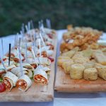 Assorted appetizers, including tortilla pinwheels and breaded bites, arranged on wooden serving boards on a white table.