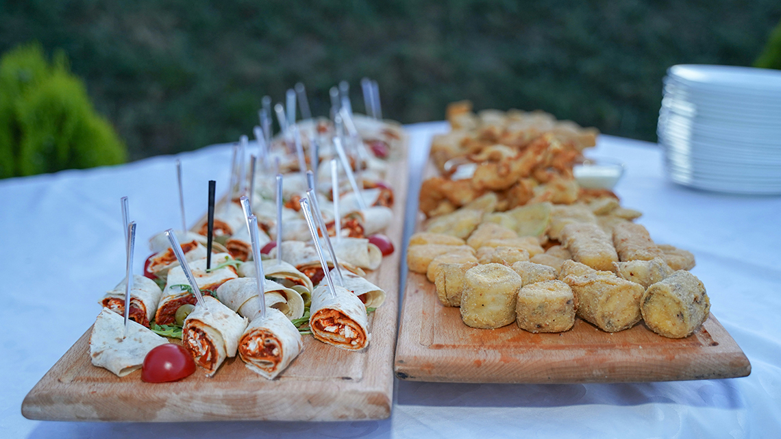 Assorted appetizers, including tortilla pinwheels and breaded bites, arranged on wooden serving boards on a white table.